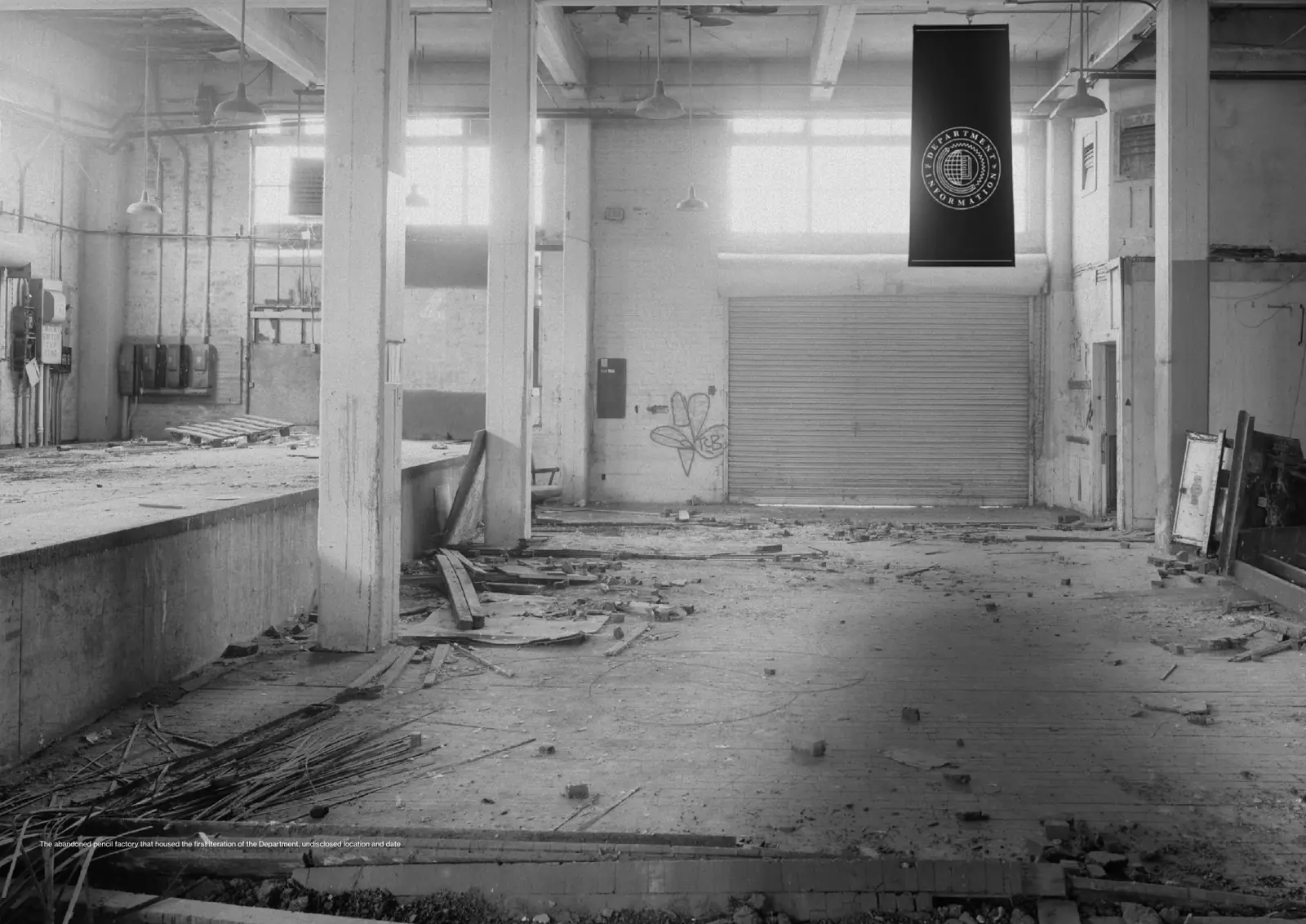 Black-and-white photograph of a derelict factory floor with a black Department banner hanging from the ceiling.